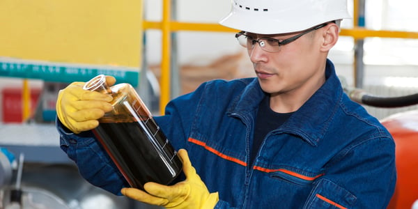A man with glasses and a hardhat holds a container of dark liquid